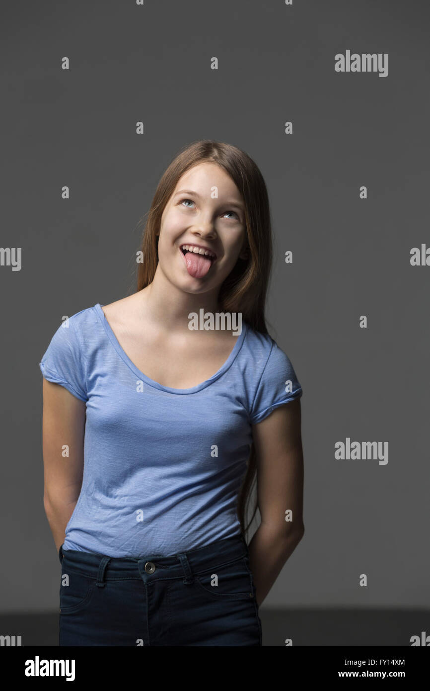 Playful girl sticking out tongue while standing against gray background Stock Photo