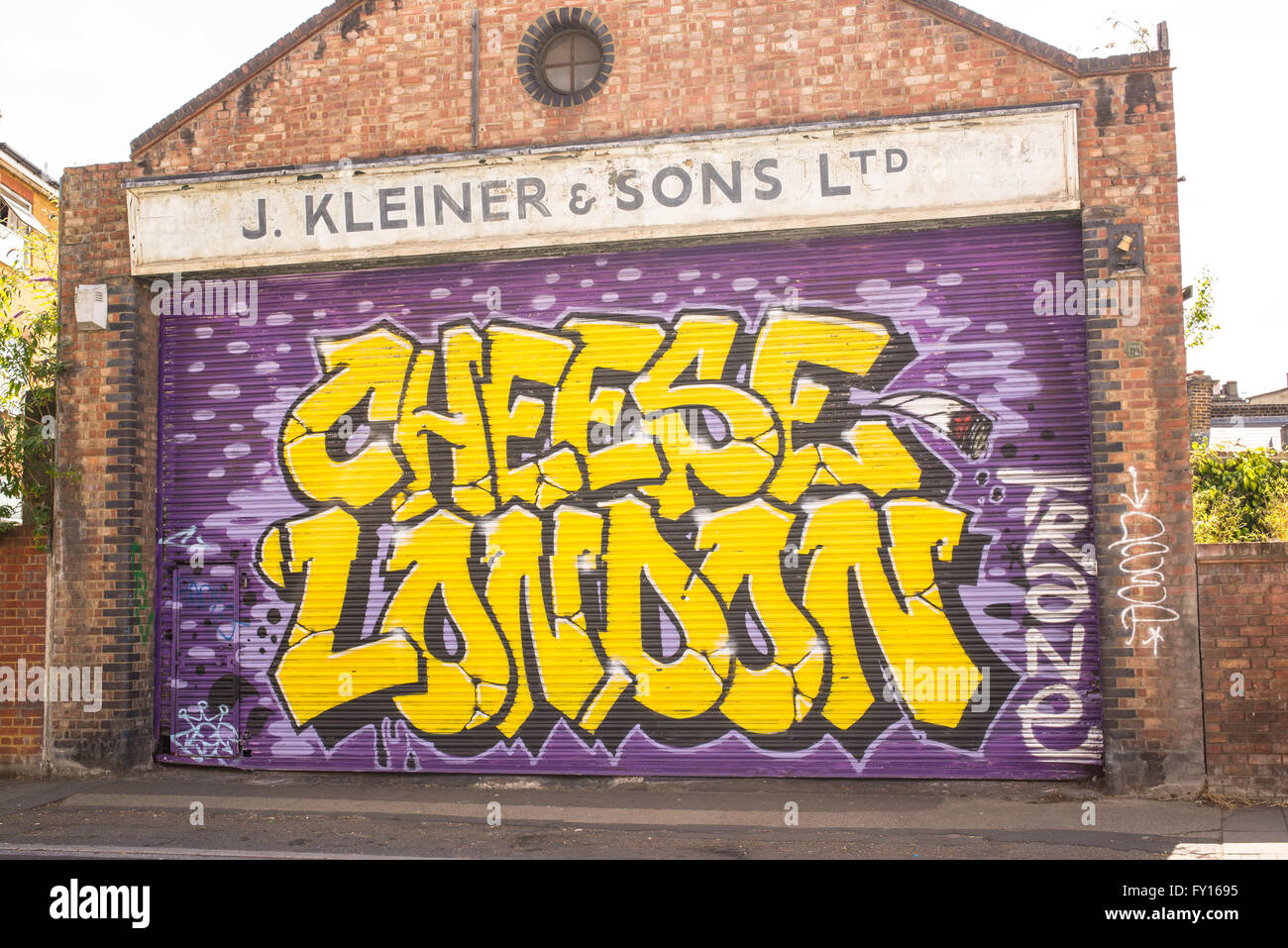 Street art mural on the garage door of an old brick building with 'Cheese London' in bright yellow letters Stock Photo