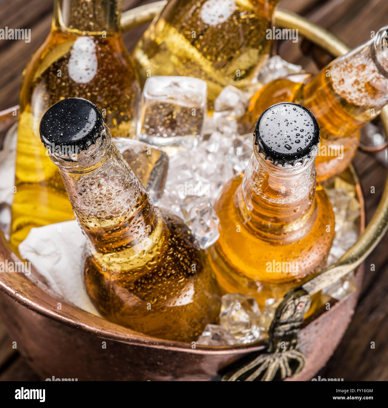 Cold bottles of beer in the brazen bucket on the wooden table. Stock Photo