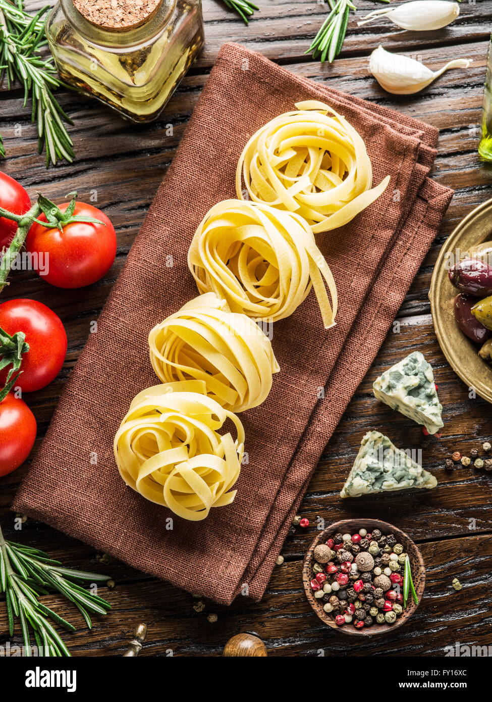 Pasta ingredients. Cherry-tomatoes, spaghetti pasta, rosemary and spices on the wooden table. Stock Photo