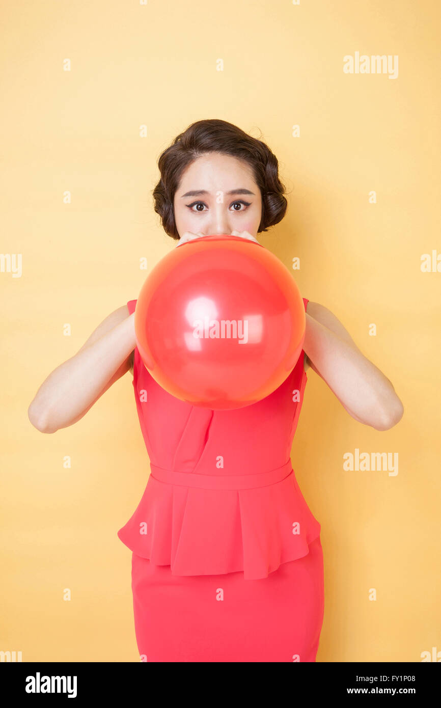 Young smiling woman in retro style blowing a balloon staring at front Stock Photo