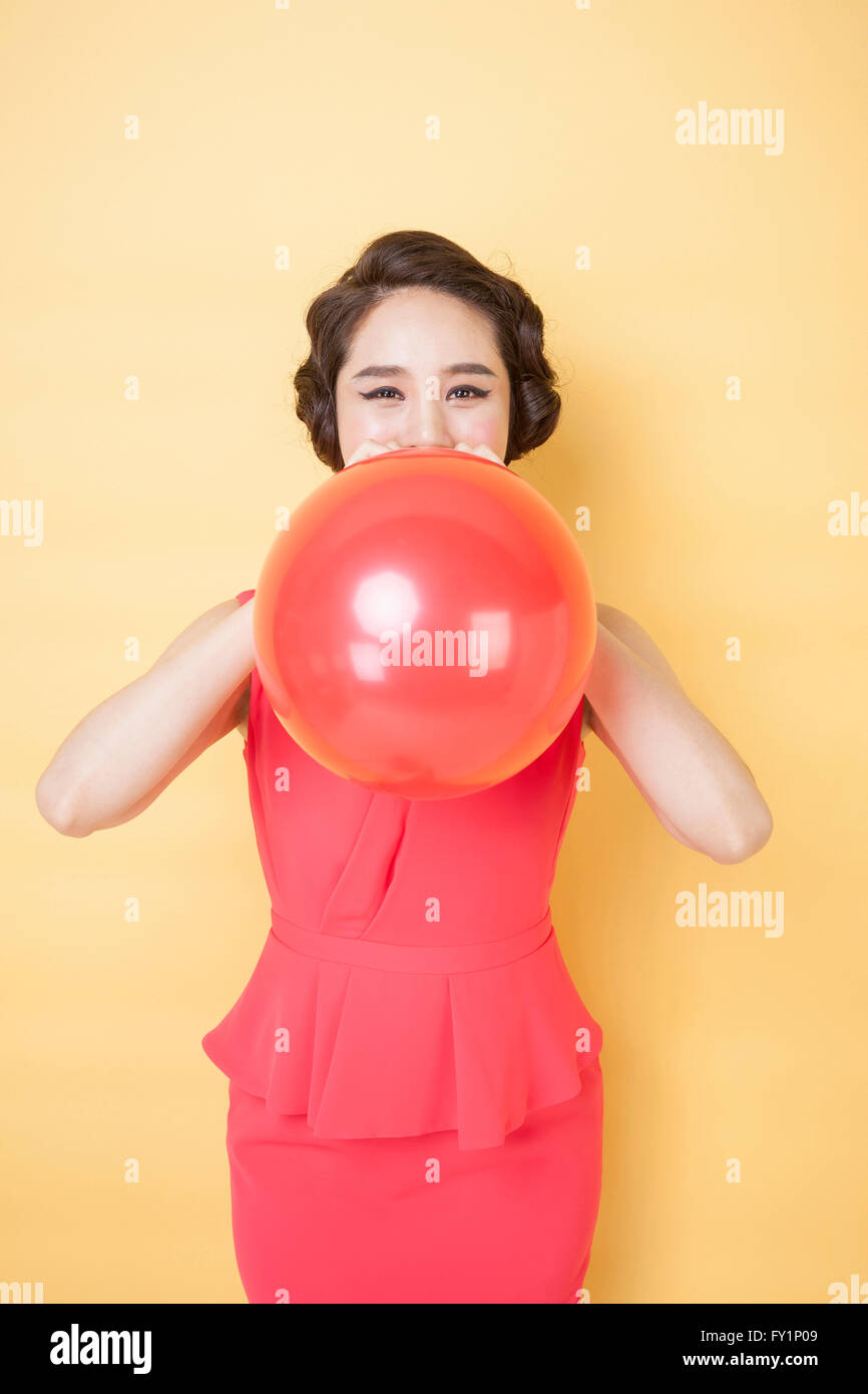 Young smiling woman in retro style blowing a balloon staring at front Stock Photo