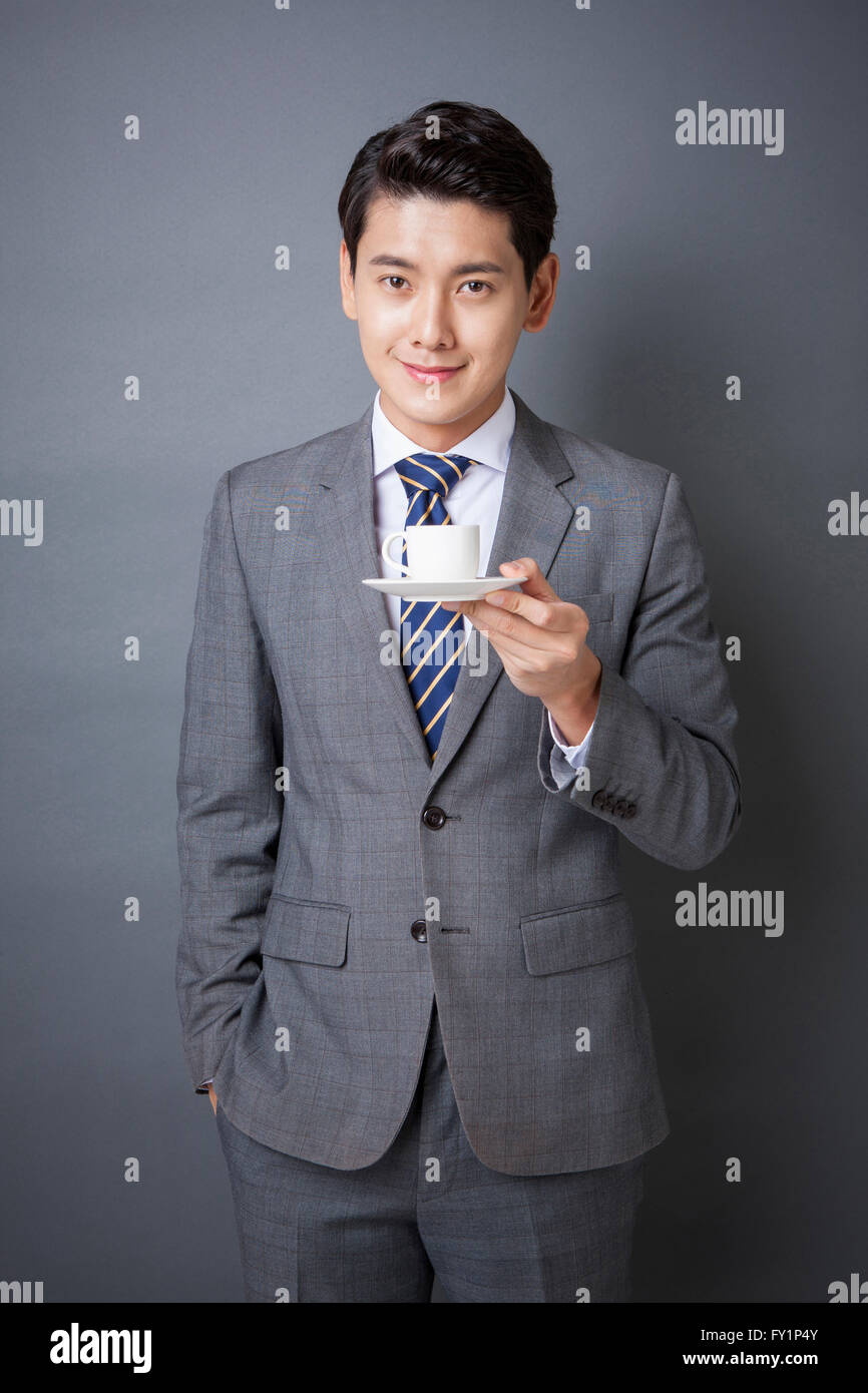 Young smiling business man in gray suit holding a cup on a saucer ...