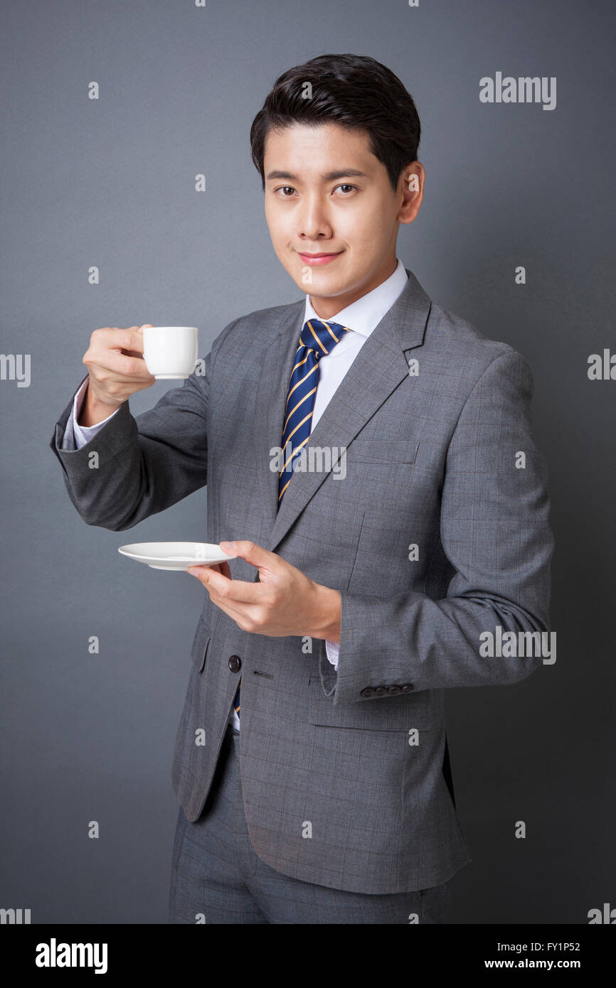 Young smiling business man in gray suit holding a cup and a saucer ...