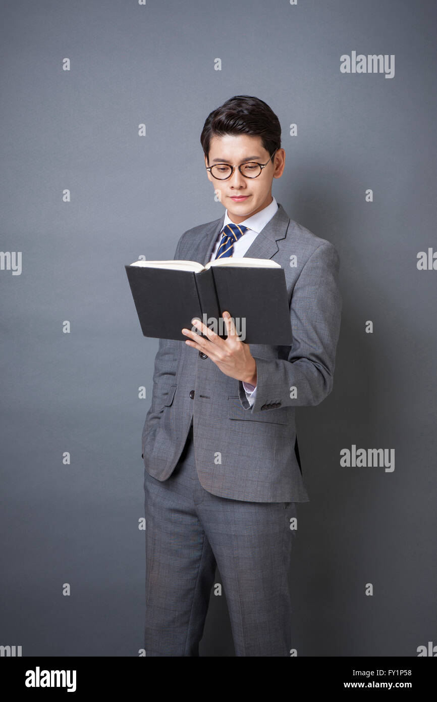Young smiling businessman in gray suit standing with a book and reading it Stock Photo