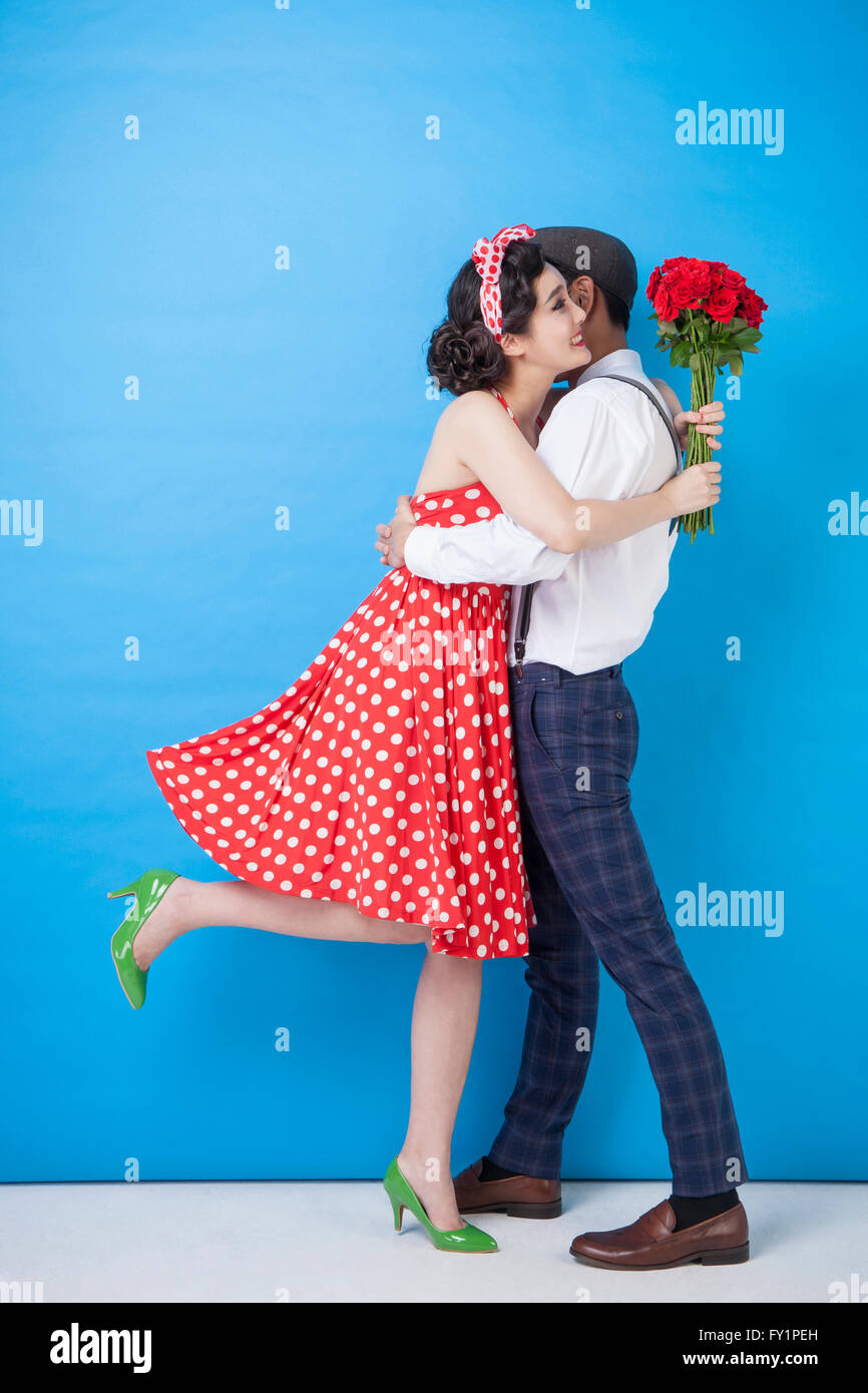 Young smiling couple in retro style standing hugging each other with red roses Stock Photo