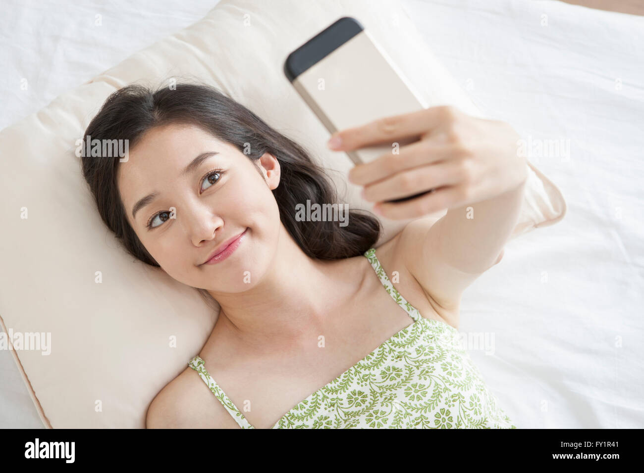Portrait of young smiling woman taking picture of herself lying down on bed Stock Photo