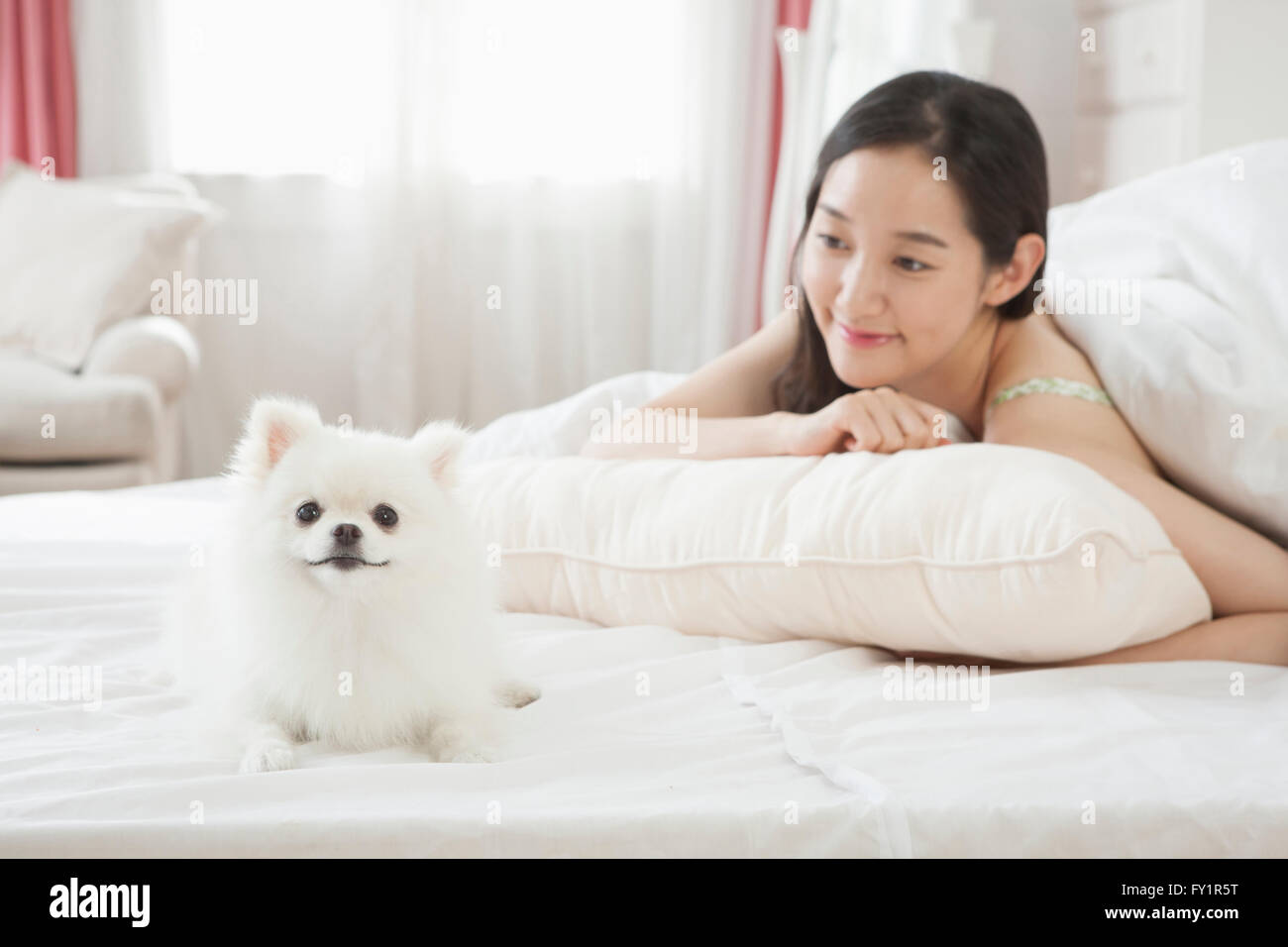 Portrait of young smiling woman lying face down in bed watching her