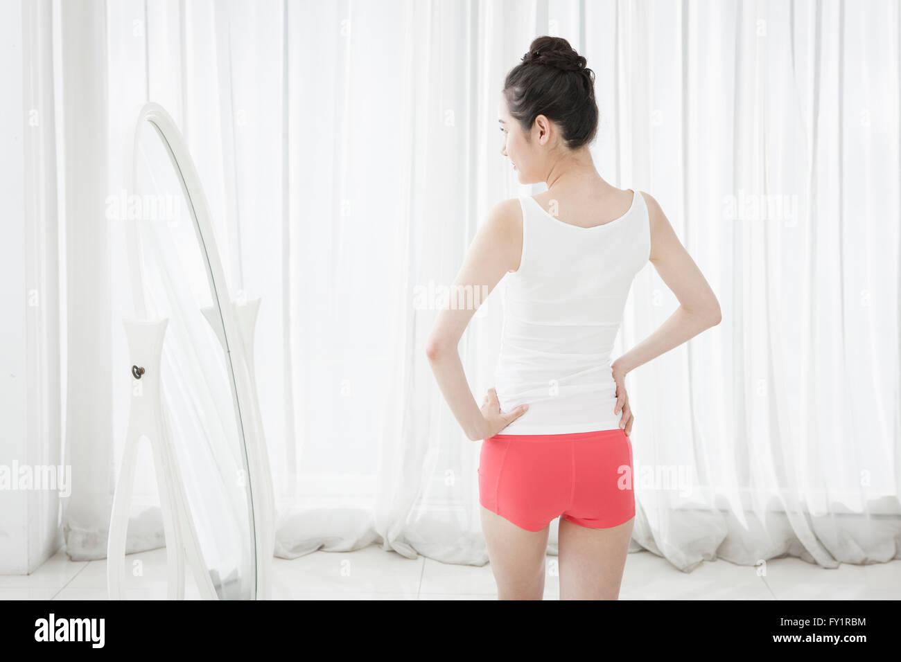 Back of young slim woman standing in front of mirror Stock Photo