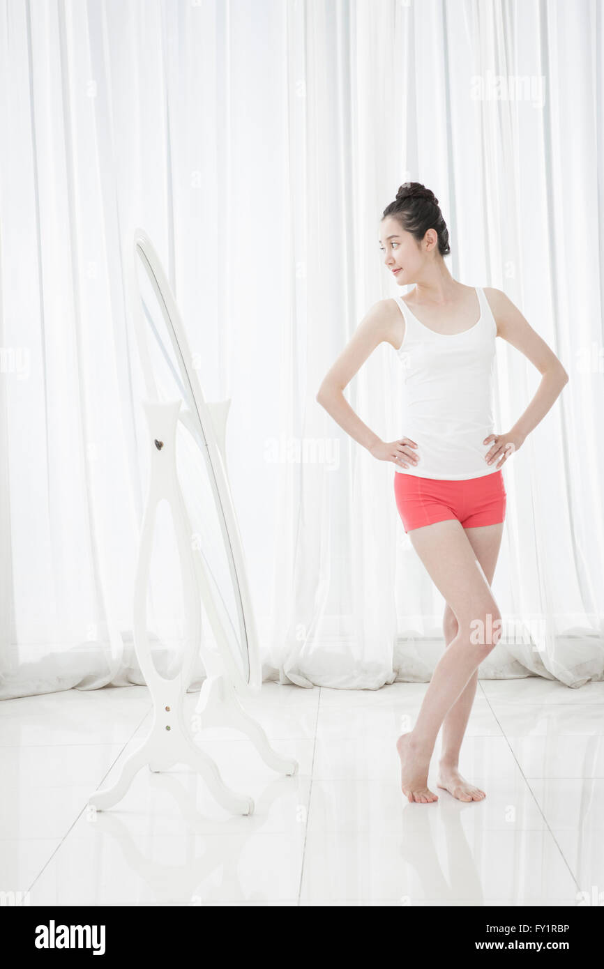 Side view of young slim woman standing and posing in front of mirror Stock Photo