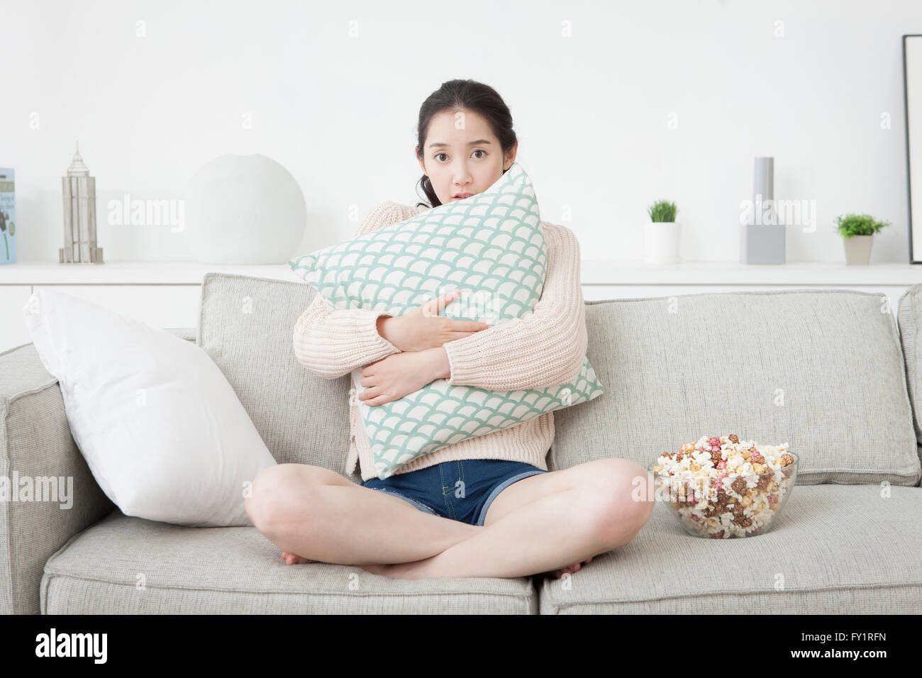https://c8.alamy.com/comp/FY1RFN/young-woman-sitting-on-sofa-hugging-a-cushion-with-frightened-face-FY1RFN.jpg