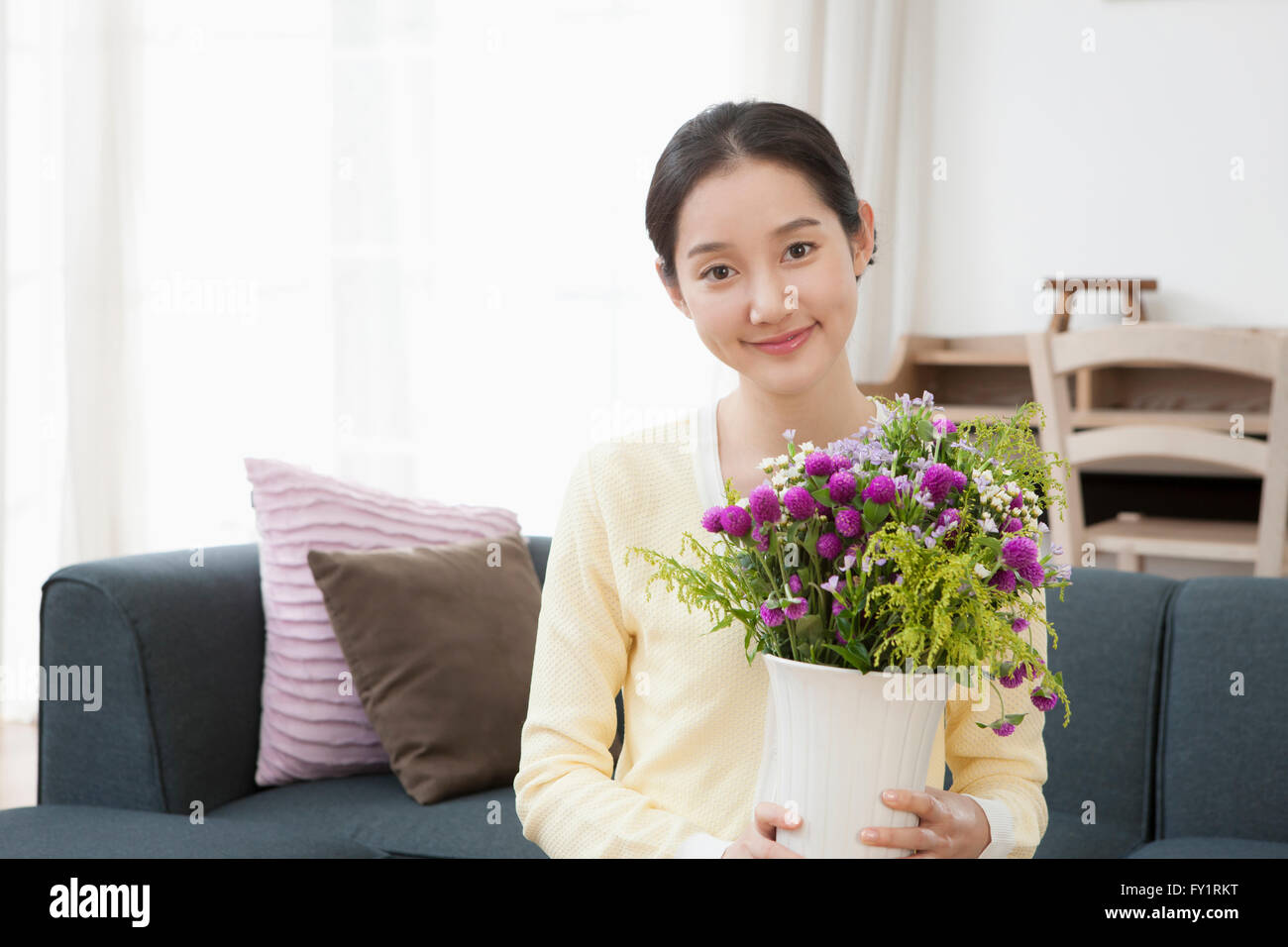 Portrait of young smiling woman holding flowers in a vase Stock Photo ...