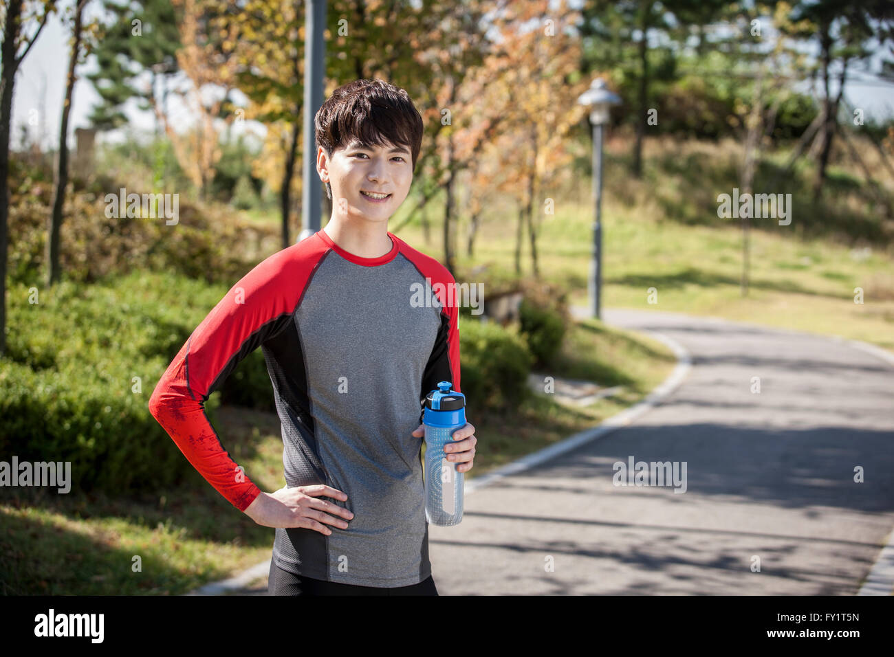 Portrait of young smiling man in sportswear posing with water bottle at ...