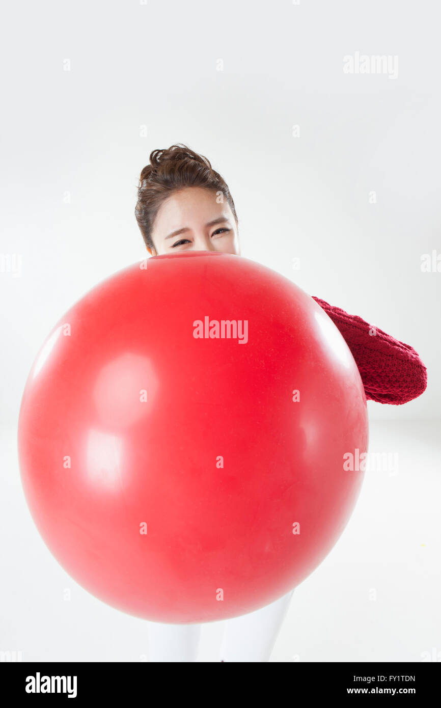 Portrait of young smiling woman blowing a big red balloon Stock Photo