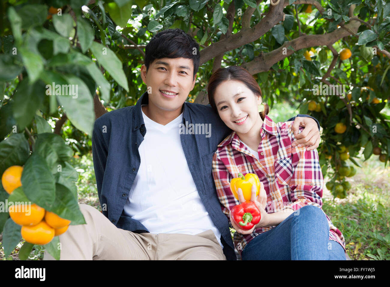 Couple with sweet peppers seated under the tangerine tree and smiling together Stock Photo