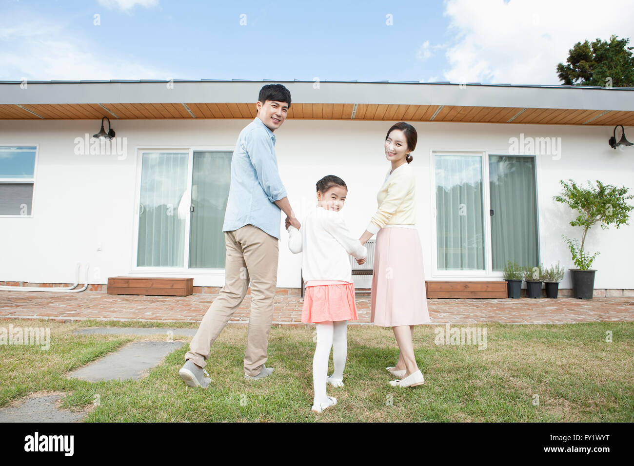 Back appearance of a family looking back and walking at the yard of their house representing rural living Stock Photo