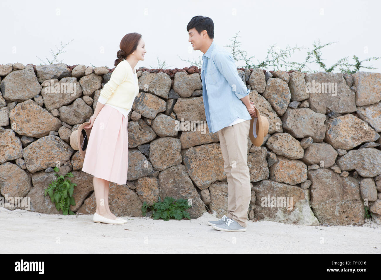 Couple facing at each other and standing by the stone wall Stock Photo
