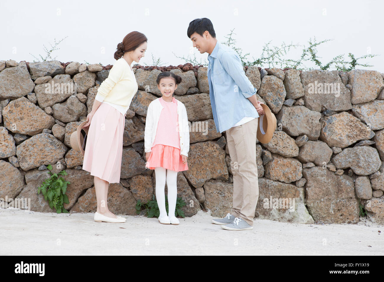 Couple facing at each other and standing by the stone wall and their daughter standing between them Stock Photo