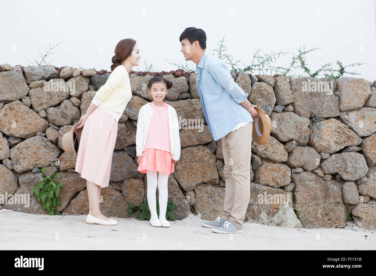 Couple facing at each other and standing by the stone wall and their daughter standing between them Stock Photo