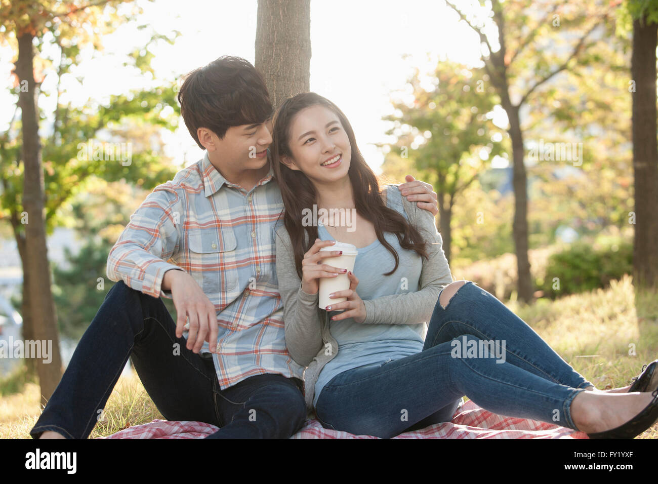 Couple seated on a grass and woman holding a cup of coffee Stock Photo