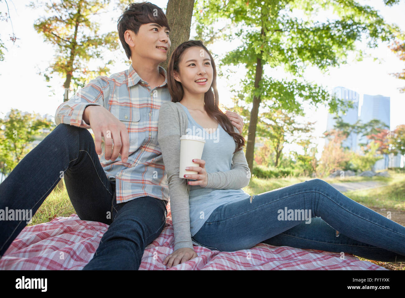 Couple seated on a grass and woman holding a cup of coffee Stock Photo
