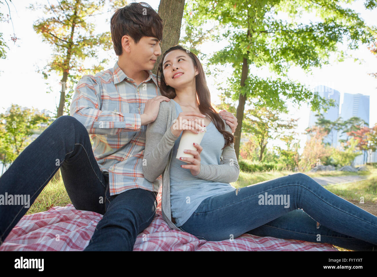 Couple seated on a grass and woman holding a cup of coffee Stock Photo