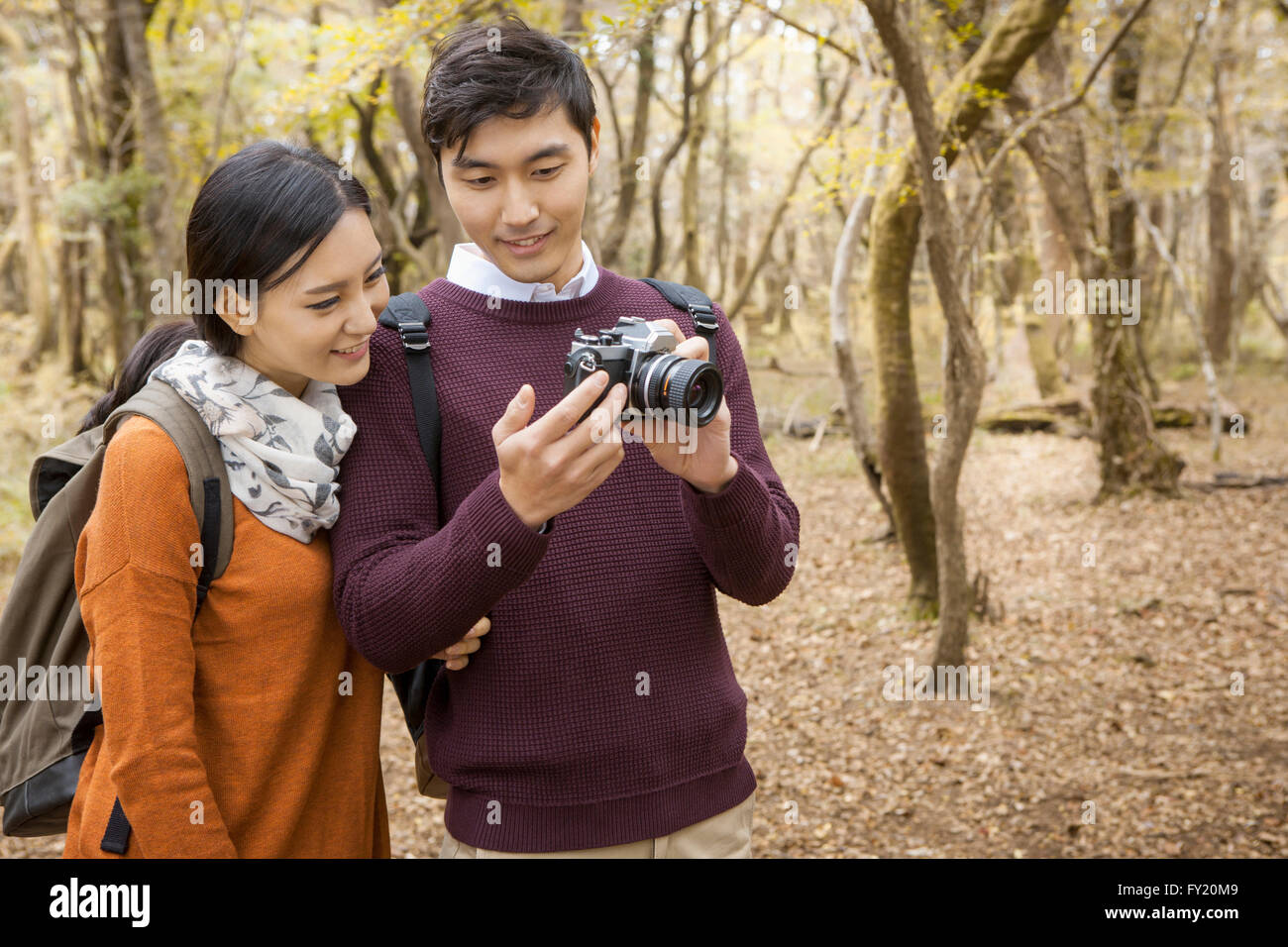 Couple in backpack looking at a camera held by the man at the forest in fall Stock Photo