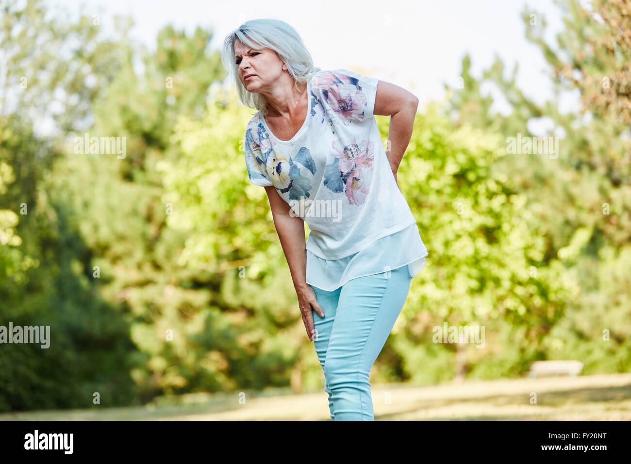 Old woman with back pain while walking in the nature in summer Stock Photo