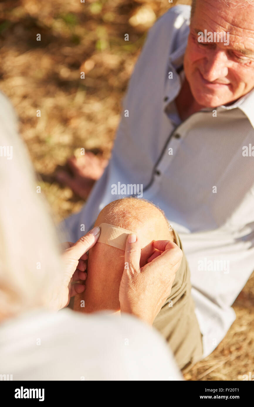 Woman sticking a plaster on the knee of an old man with knee injury Stock Photo