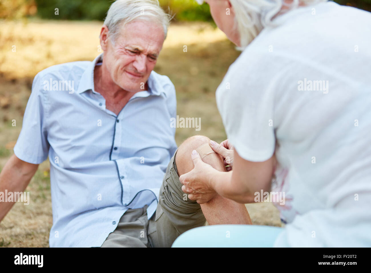 Old man with pain on his knee and woman gives him first aid Stock Photo