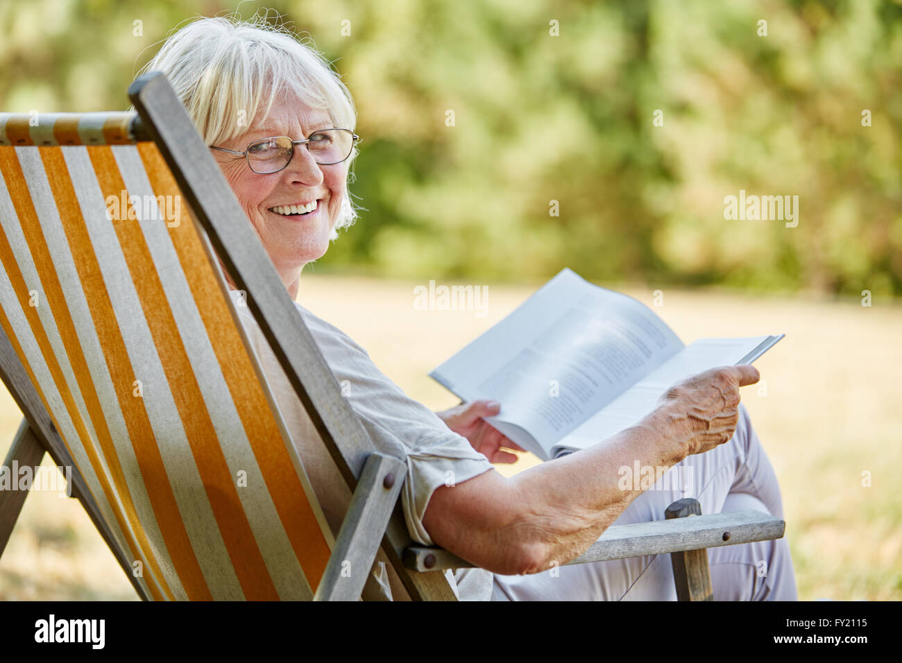 Old happy lady reading a book and smiling in summer in the nature Stock Photo