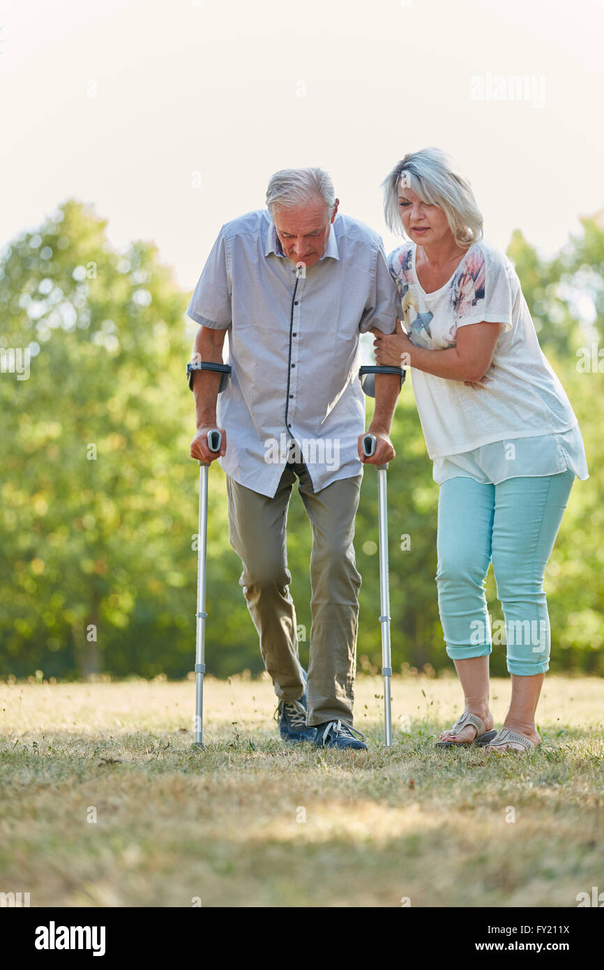 Old man lerns to walk with crutches in the nature with help from his