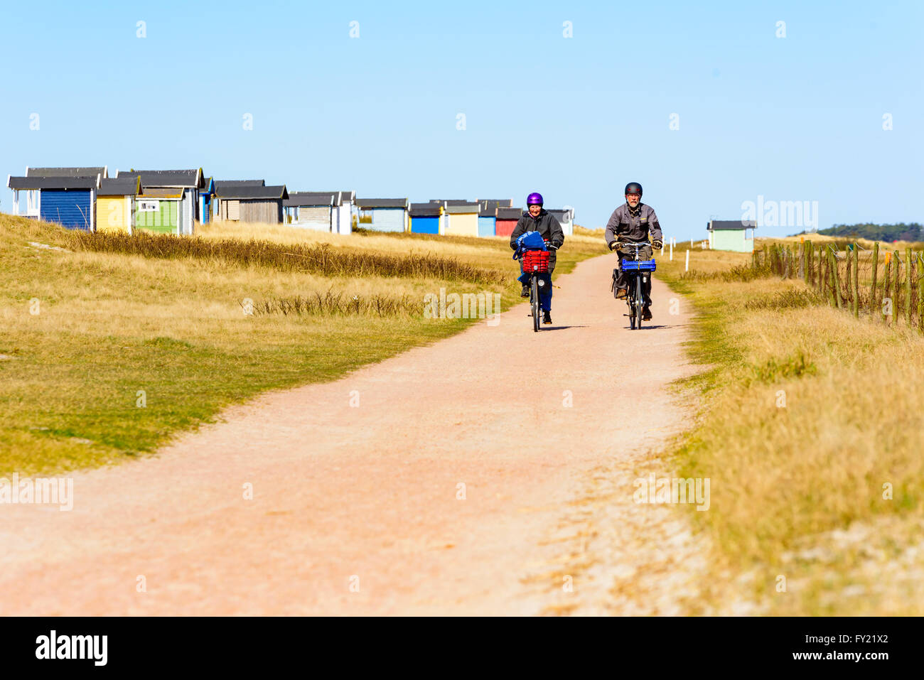 Skanor, Sweden - April 11, 2016: A senior couple is out riding bikes on the road at the beach along some bathing cabins. Both we Stock Photo