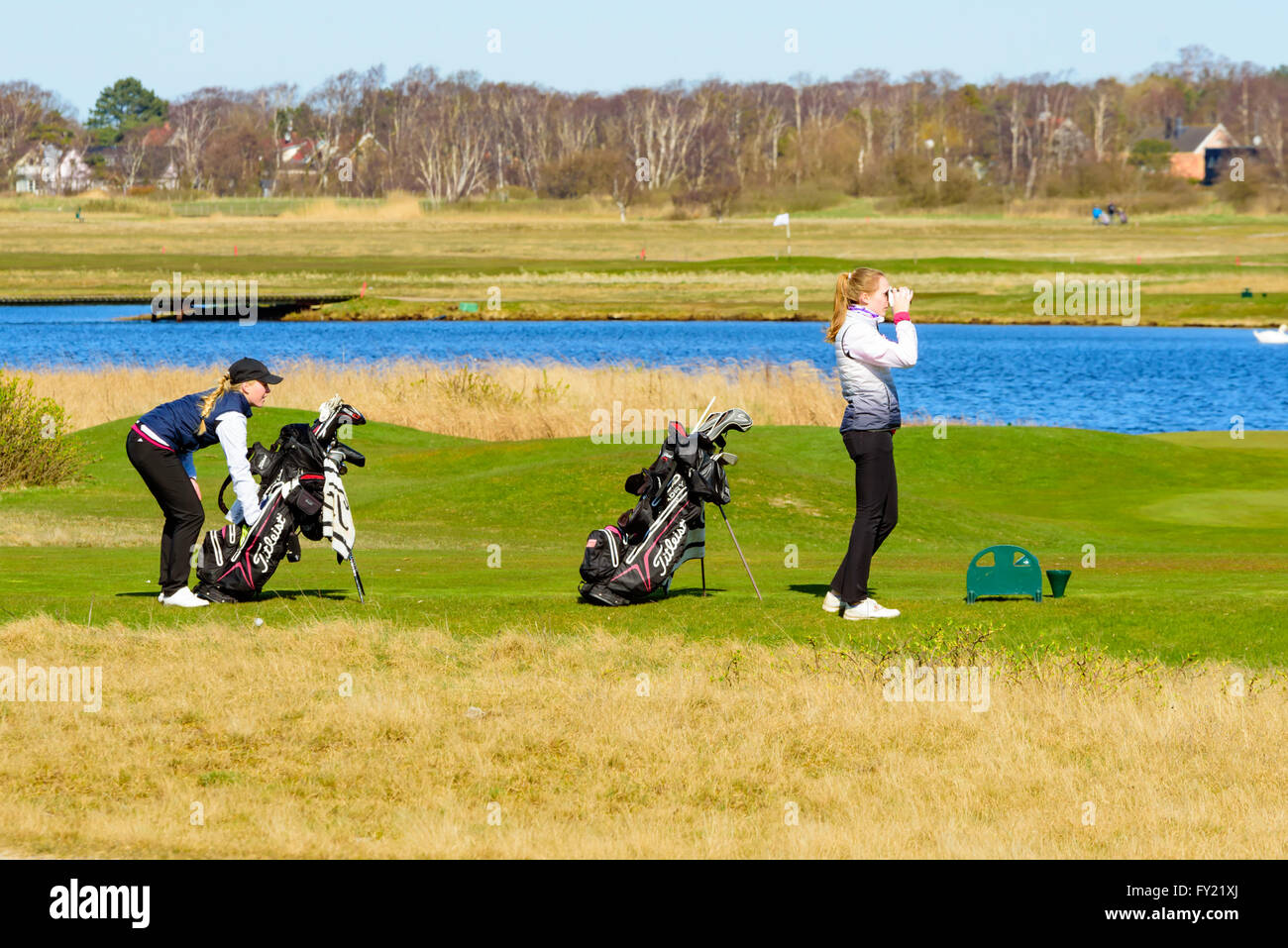 Skanor, Sweden - April 11, 2016: Two young female golfers look away into the distance to see how a ball played out on the course Stock Photo