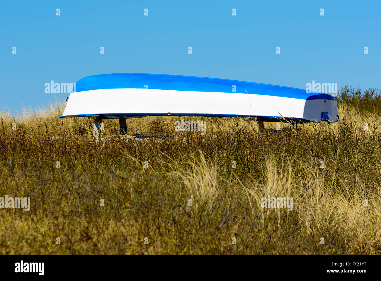 Blue and white upside down boat in the dry grass at the beach. Stock Photo