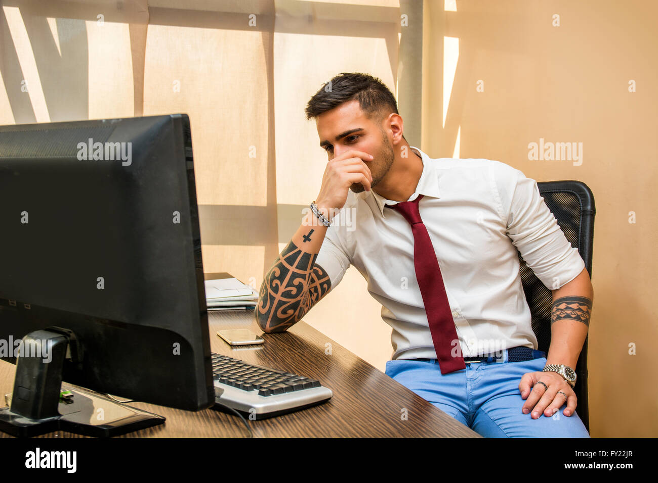 Tired or frustrated, worried young man working in office looking at computer screen Stock Photo
