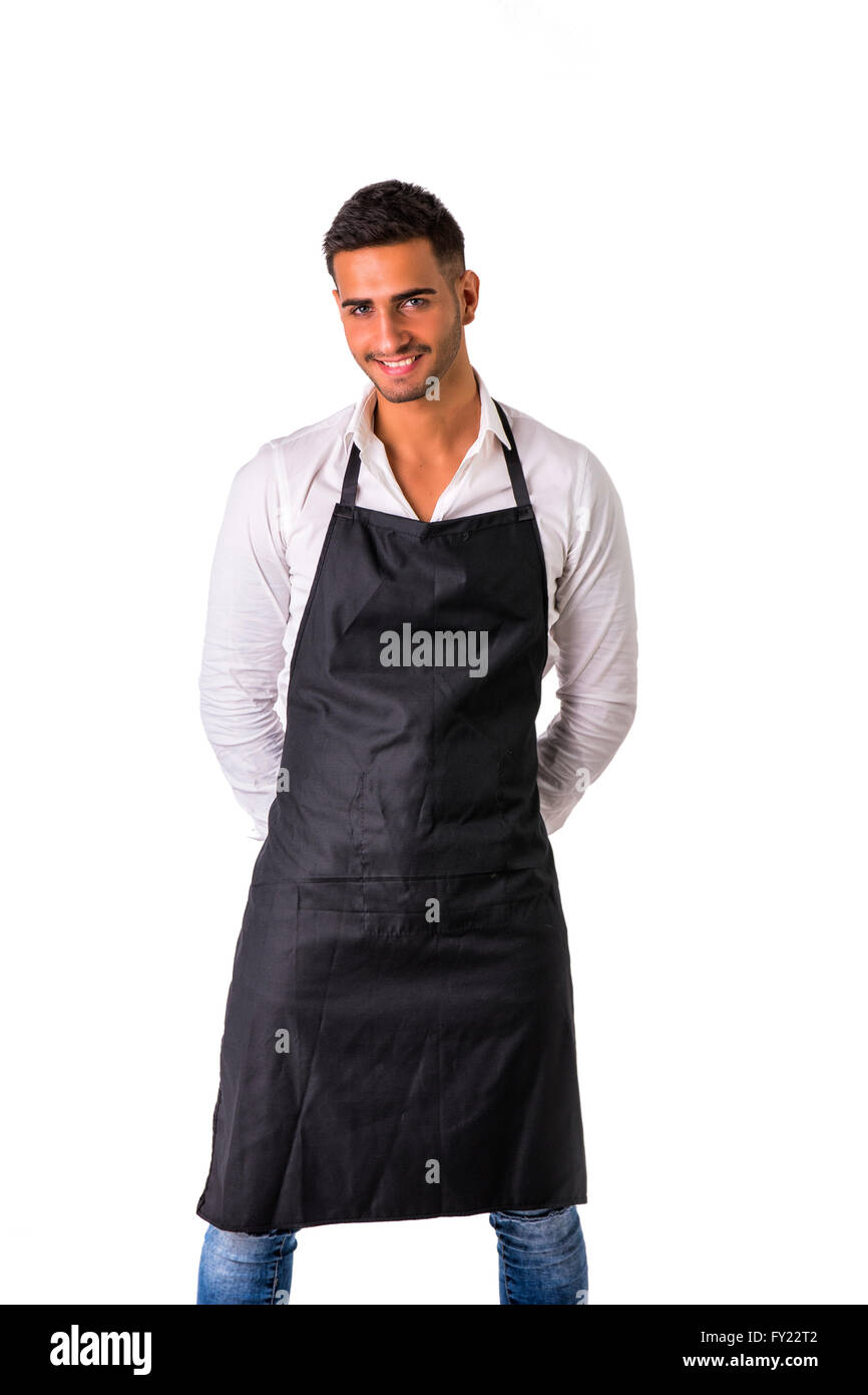 Young chef or waiter posing, welcoming guests with a smile, wearing black apron and white shirt isolated on white background Stock Photo