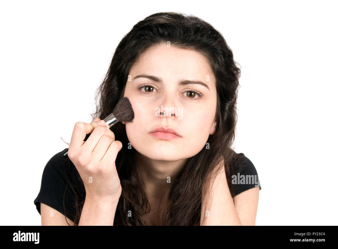 Young woman uses a cosmetic brush to apply blush makeup to her face. Stock Photo