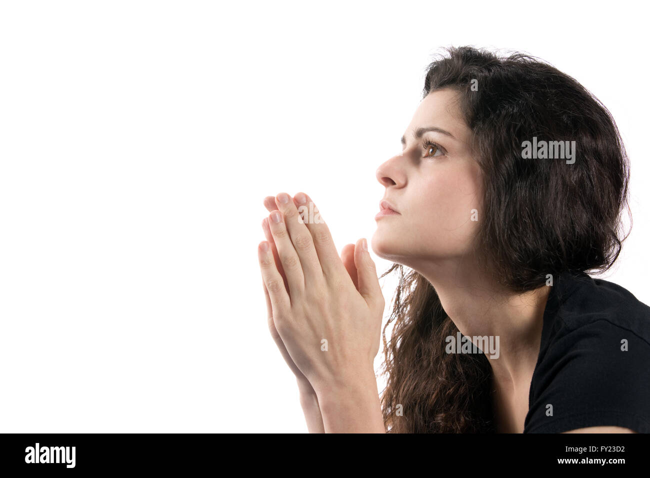 Woman prays while looking up with her hands together. Stock Photo