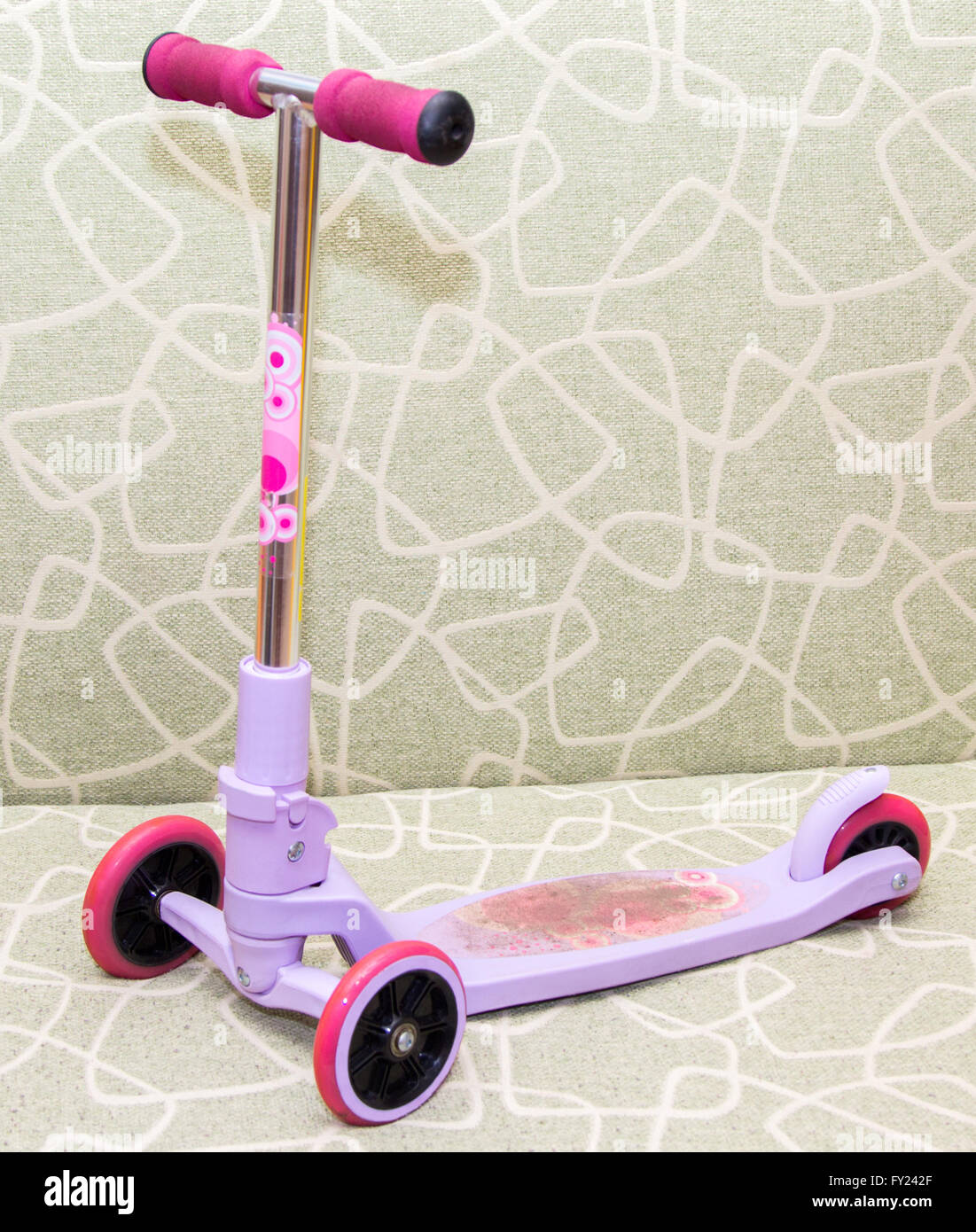 small three-wheeled children pink scooter on the couch Stock Photo