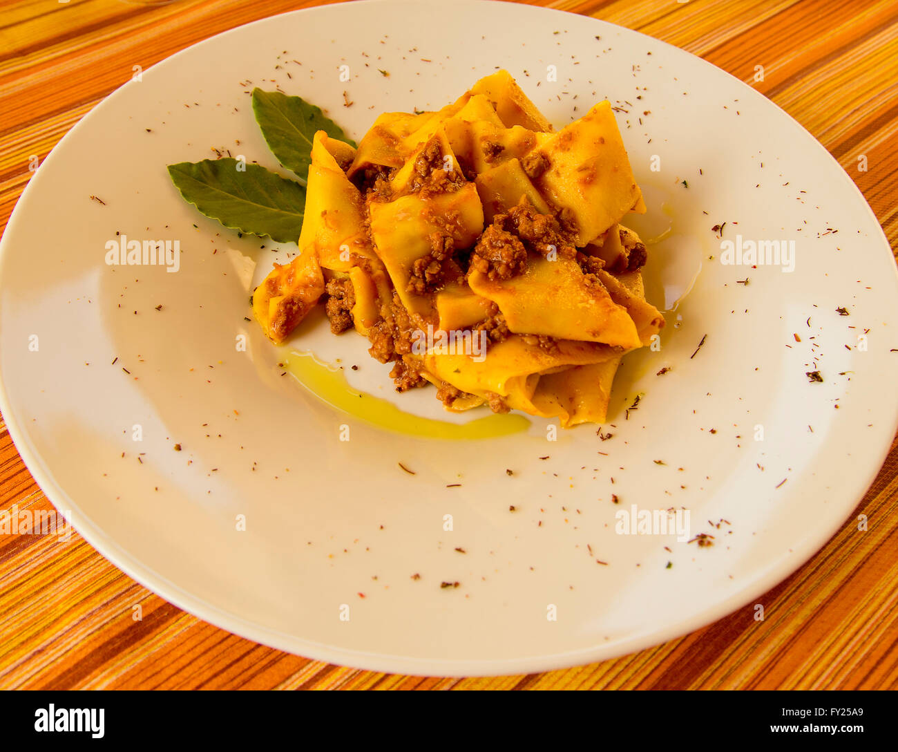 Italian pasta dish on a white plate pappardelle con ragu di cinghiale wild boar olive oil bay leaf Italian food cooking in Italy Stock Photo
