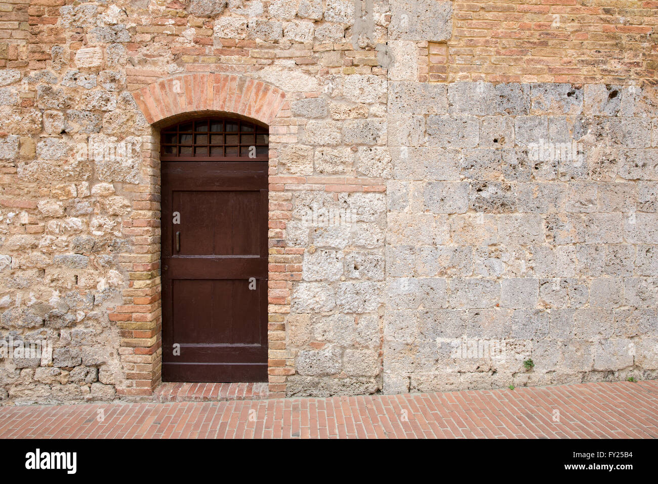 Brown door in a medieval stone and brick wall in the Tuscan village of ...