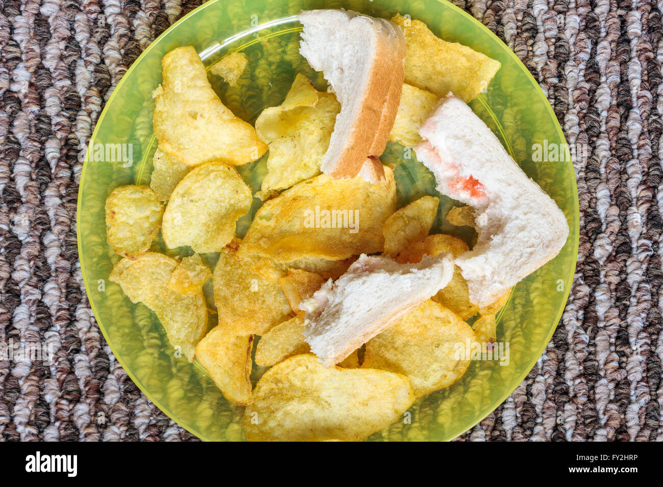 Crisps and crusts from a half eaten sandwich left over on a child's plastic plate Stock Photo