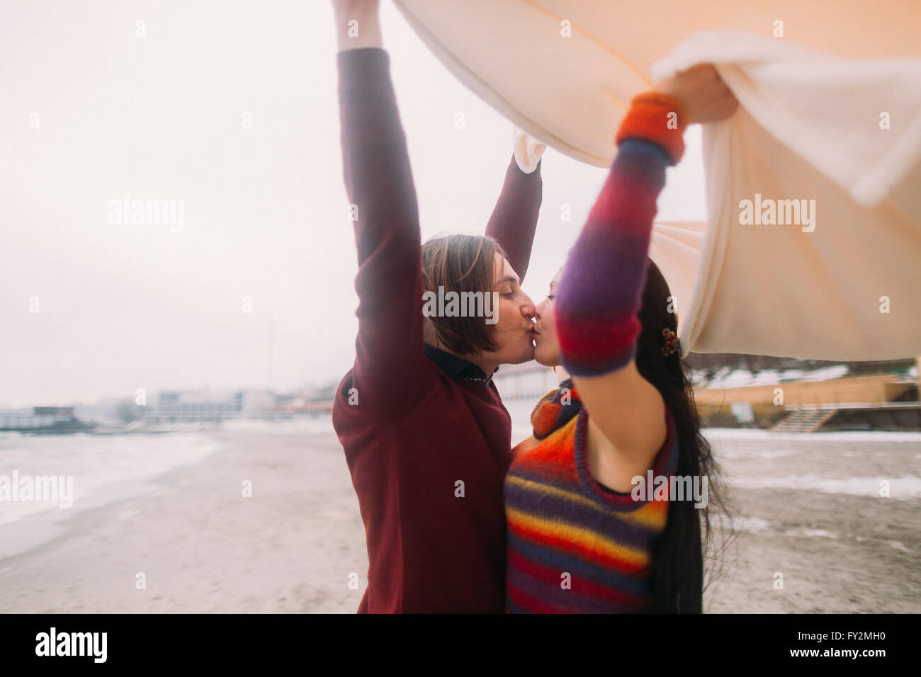 Attractive bright young happy couple kissing under white blanket on the