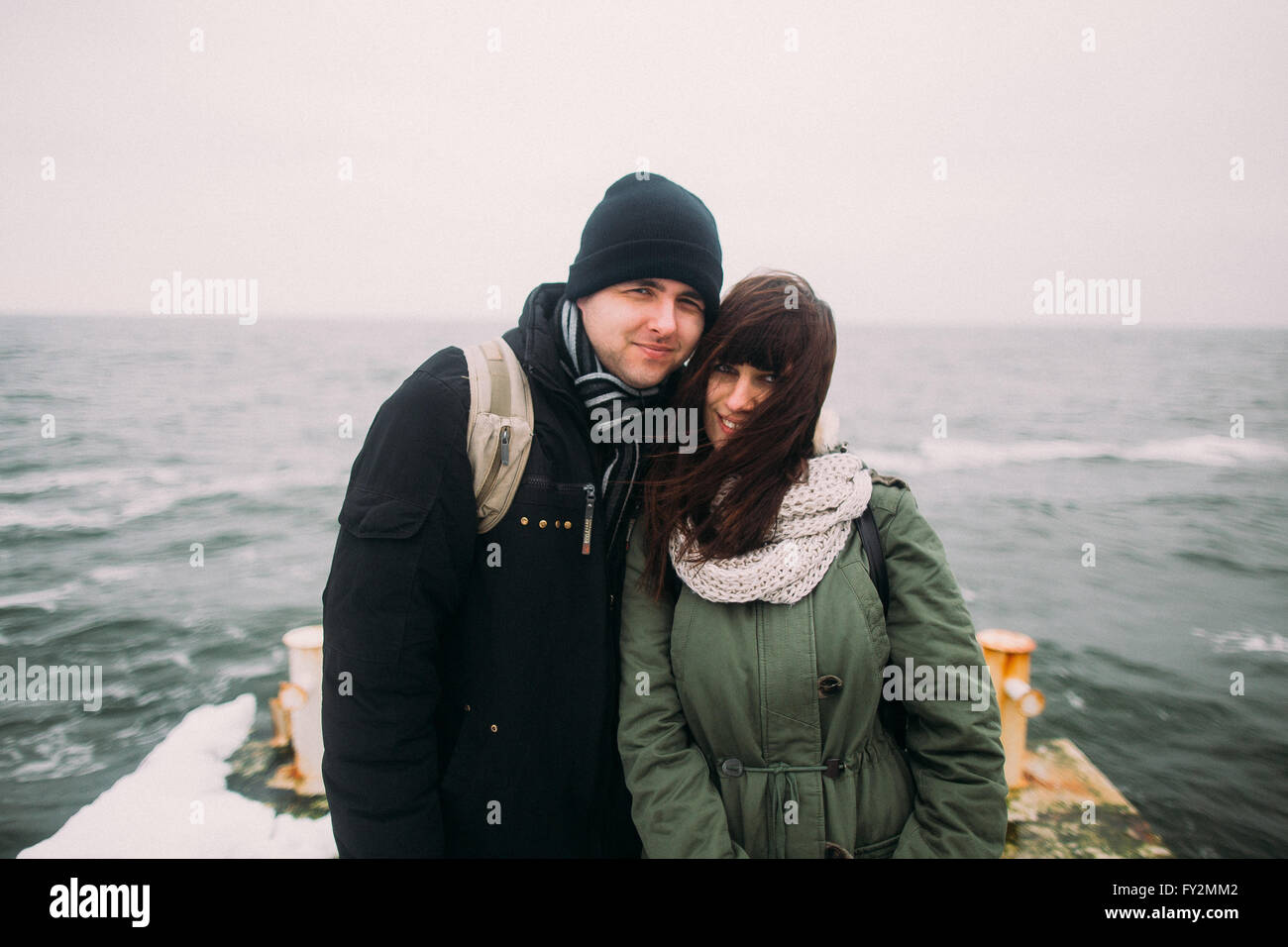 Portrait of urban fashion stylish couple posing and holding hands on the old pier in winter vacation. Travel together concept. Sea background Stock Photo