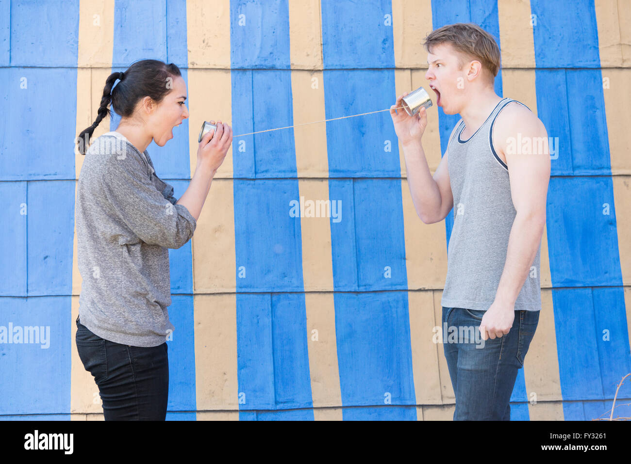 Young woman and young man with a tin can phone, both shouting into it, conceptual image of communication in a relationship Stock Photo