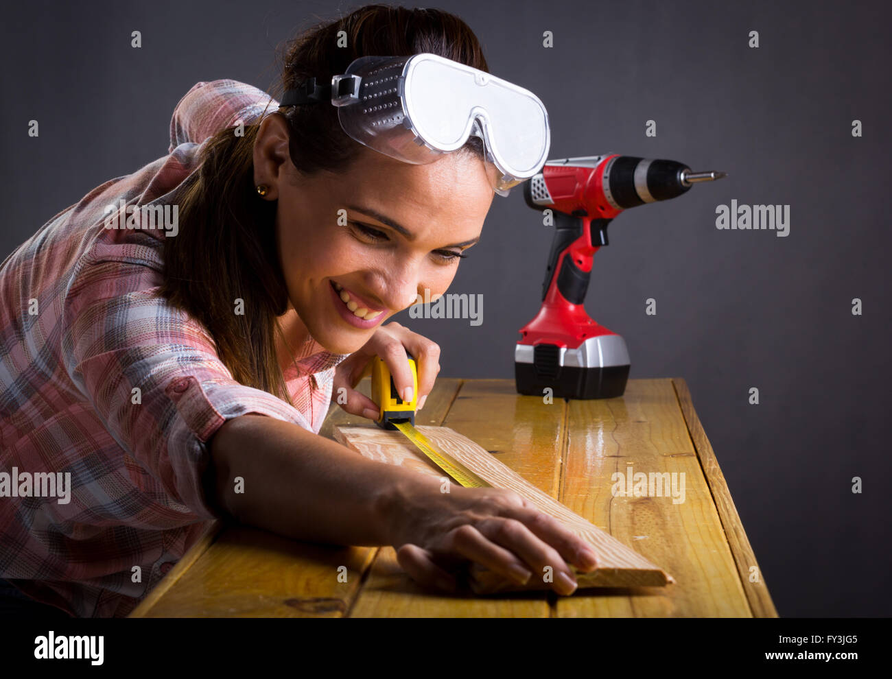 Young adult Hispanic woman measuring a wooden board with a tape measure Stock Photo