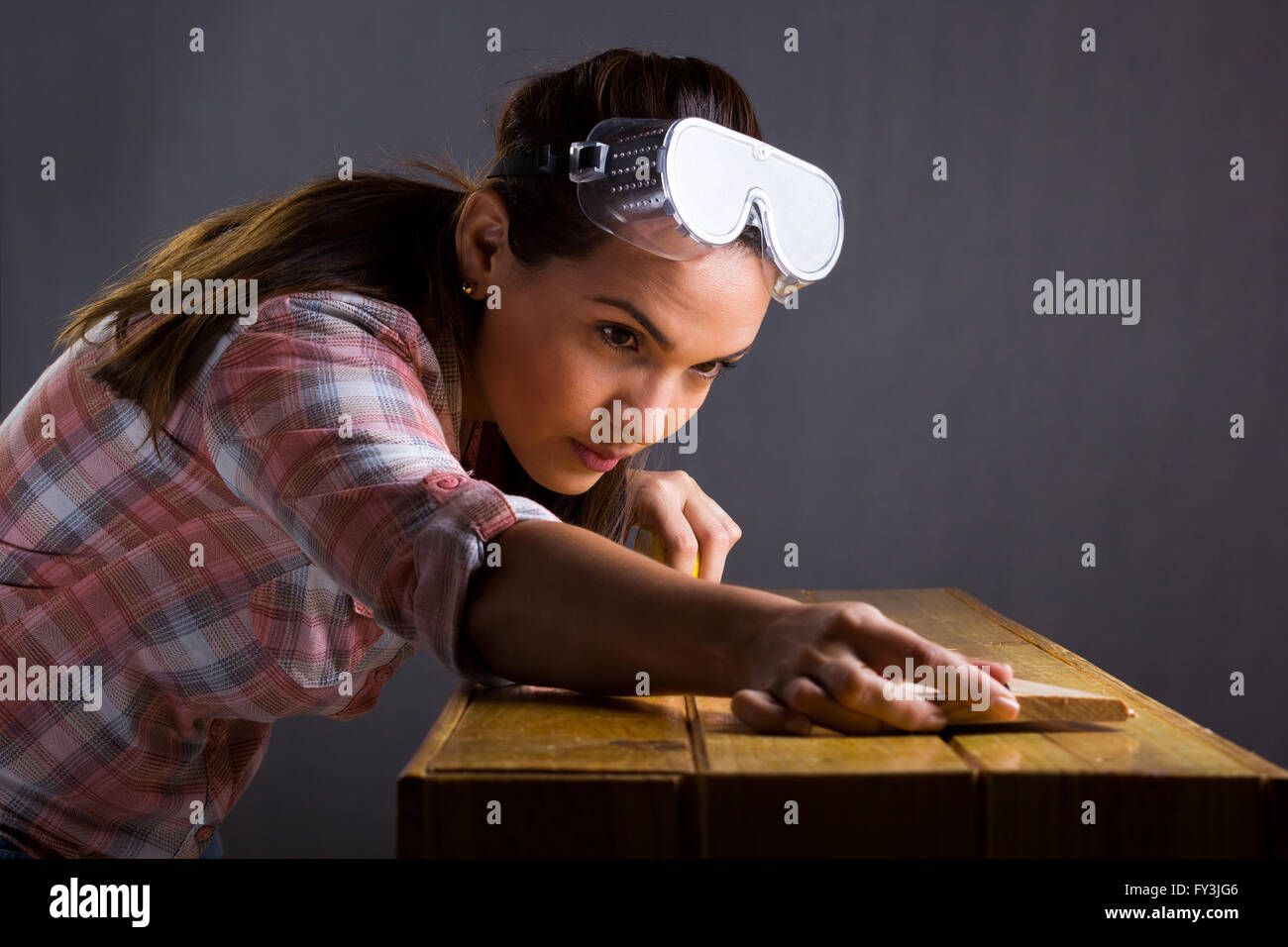 Young adult Hispanic woman measuring a wooden board with a tape measure Stock Photo
