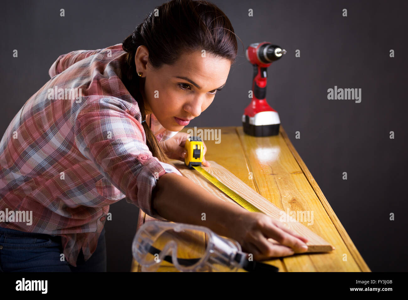 Young adult Hispanic woman measuring a wooden board with a tape measure Stock Photo