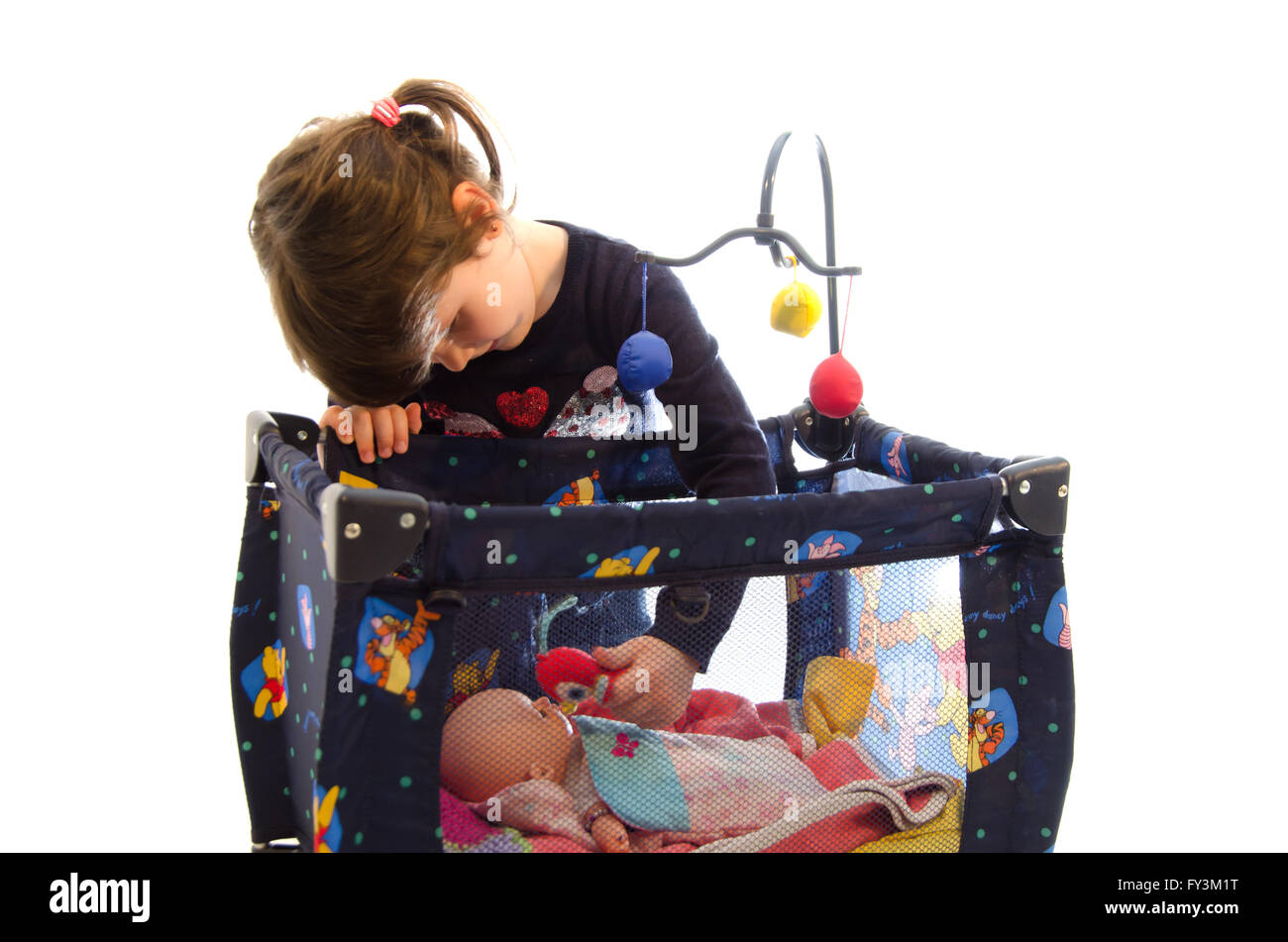 Sweet toddler girl taking care of a baby in his toy bed isolated on white background Stock Photo